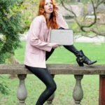 woman in pink blazer and black pants sitting on brown wooden bench